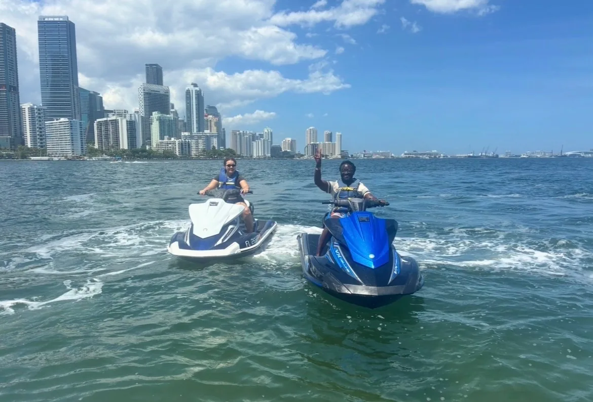 Two jet ski riders waving in front of downtown Miami skyline on Biscayne Bay